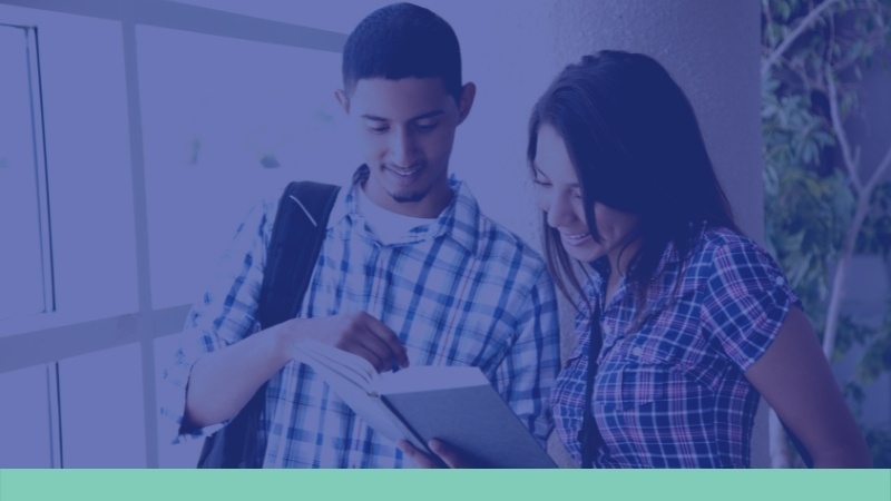 Image of two students standing in a hallway reading a book