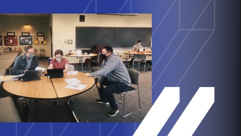 Image of two students sitting with advisor at a table in a classroom over a royal blue background with white MCAN logo in bottom right