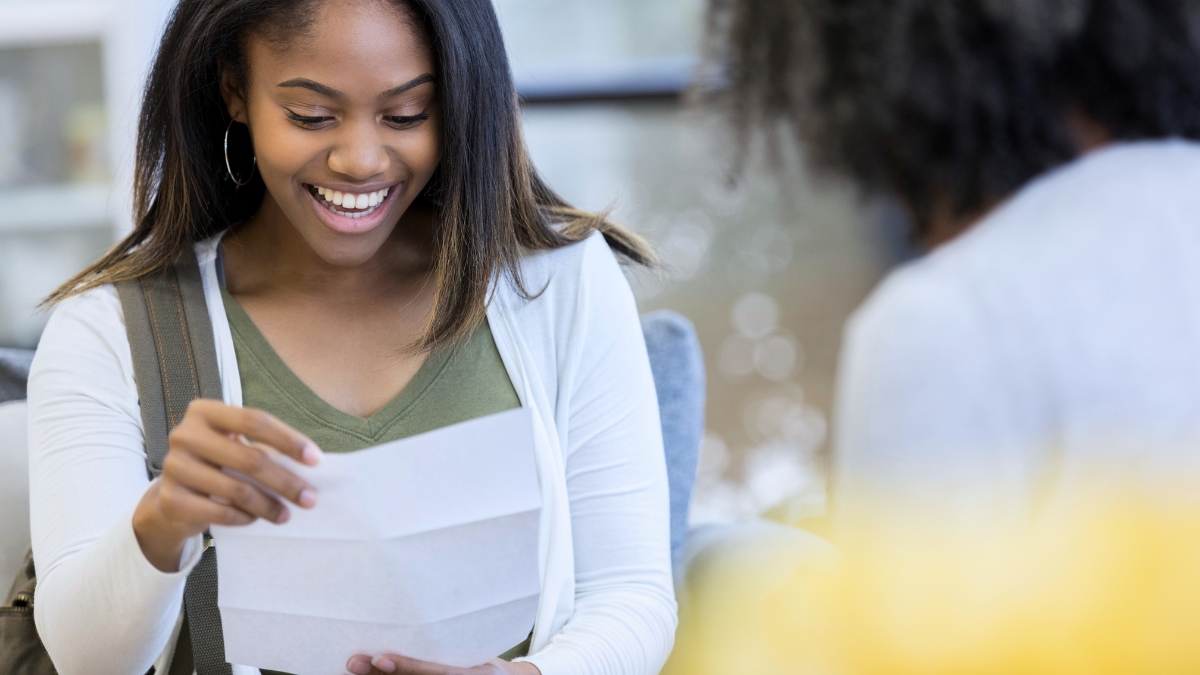 A young Black women reading a letter while another person looks on.